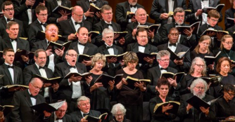 A large choir from Voices of Omaha performing onstage, singing together under bright concert lighting.