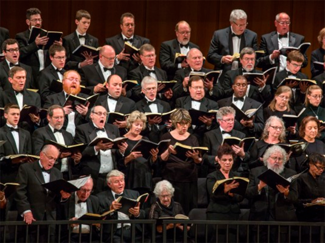 A large choir from Voices of Omaha performing onstage, singing together under bright concert lighting.