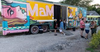 People walk around the BFF Mobile Gallery trailer, exploring artwork displayed inside and outside the mobile exhibition space