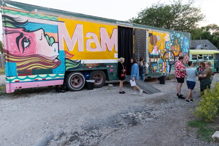 People walk around the BFF Mobile Gallery trailer, exploring artwork displayed inside and outside the mobile exhibition space