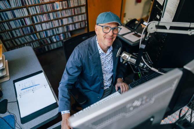 Jeff Koterba sitting in front of a microphone in the KVNO studio, smiling at the camera.
