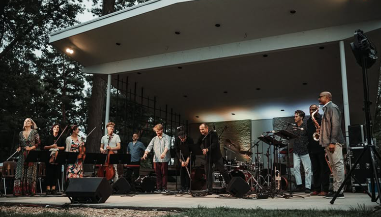 A group of performers on stage at the Nebraska Crossroads Music Festival, playing instruments and singing for the audience.