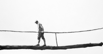 Painting titled The Space in Between by Josephine Langbehn, depicting a solitary man walking across a hanging bridge.