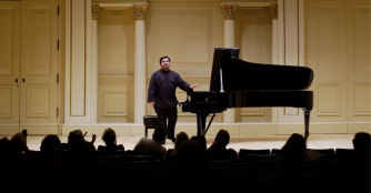 Pianist Marcelo Lian stands next to a grand piano after a concert, smiling and reflecting on a successful performance.