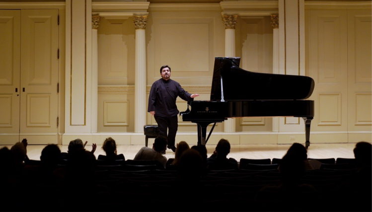 Pianist Marcelo Lian stands next to a grand piano after a concert, smiling and reflecting on a successful performance.