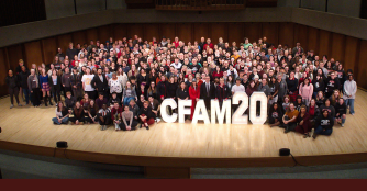 Students, faculty, and staff from the College of Communication, Fine Arts, and Media gathered onstage around a large “CFAM20” sign.