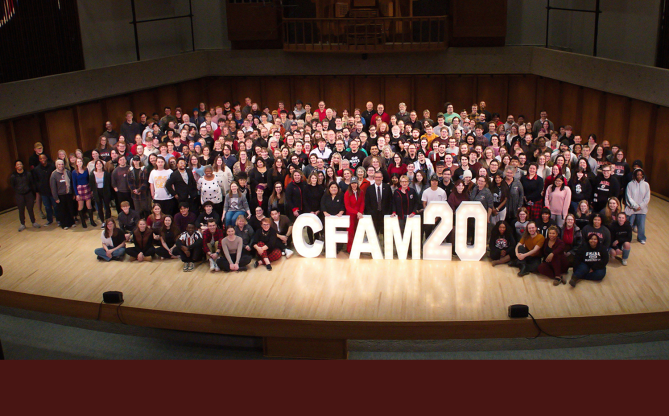 Students, faculty, and staff from the College of Communication, Fine Arts, and Media gathered onstage around a large “CFAM20” sign.