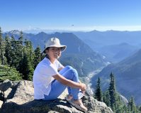 Clair Wang sitting on a rock in front of a mountain range.