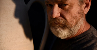 Rodney Tague smiling while posing in front of his pottery work, representing Clay Contours.