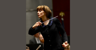 Grammy-winning conductor JoAnn Falletta leading an orchestra with focused intensity, baton raised mid-gesture as she directs musicians during a performance.