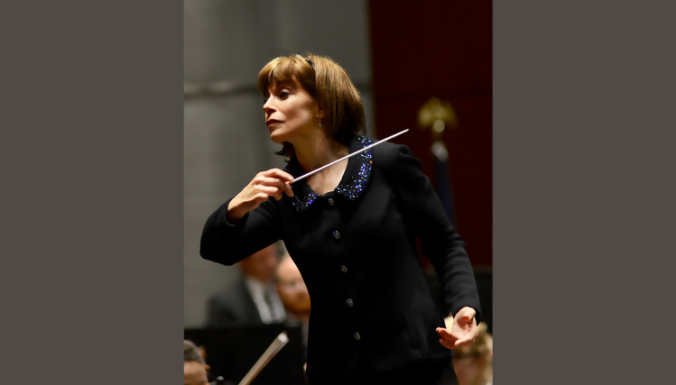 Grammy-winning conductor JoAnn Falletta leading an orchestra with focused intensity, baton raised mid-gesture as she directs musicians during a performance.