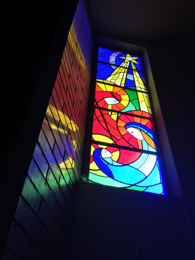 A tall stained-glass window designed by Julee Lowe with a Nativity theme