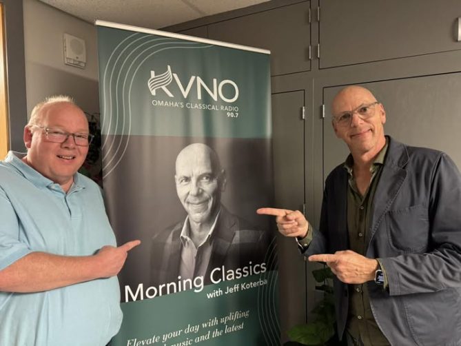 Jeff Koterba and Matt Barnett pointing at a banner with a picture of Jeff on it. 