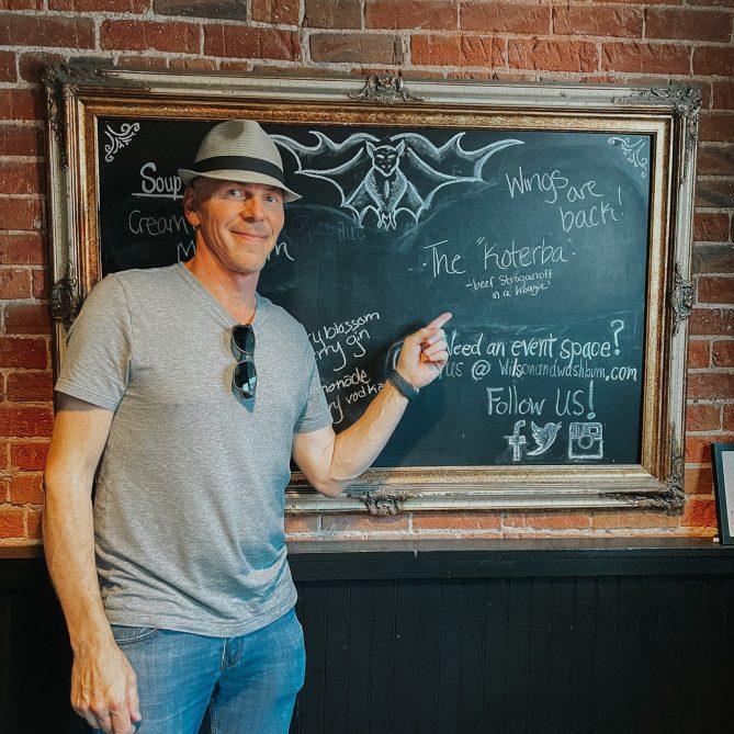 Jeff Koterba pointing to a chalkboard at Omaha restaurant, Wilson & Washburn, that is promoting the "Koterba" sandwich.
