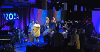 Interior of NOMA Café featuring cozy lighting, tables arranged for live jazz, and musicians performing on stage.