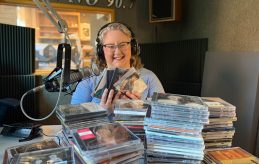 KVNO music director, Emily McIvor in front of stacks of CDs