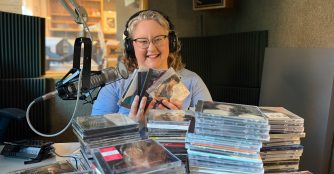 KVNO music director, Emily McIvor in front of stacks of CDs