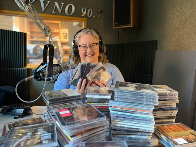 KVNO music director, Emily McIvor in front of stacks of CDs