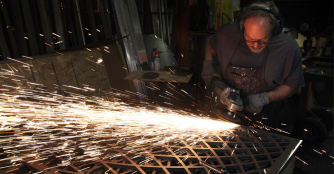 An artist uses a metal grinder, sending sparks flying while working on a sculpture at the Hot Shops Art Center in Omaha.