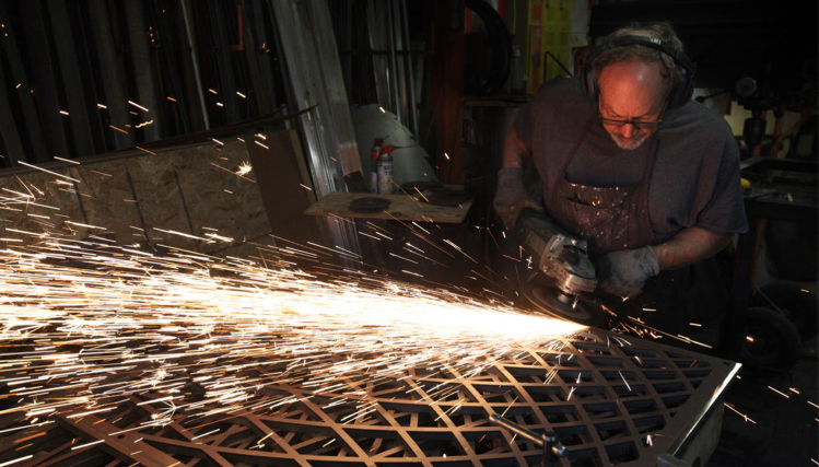 An artist uses a metal grinder, sending sparks flying while working on a sculpture at the Hot Shops Art Center in Omaha.