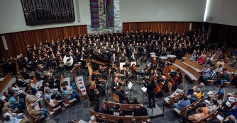 Baron Breland conducts a choir during a live performance, leading singers with expressive gestures.