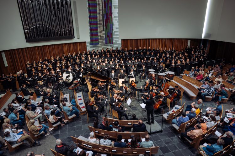 Baron Breland conducts a choir during a live performance, leading singers with expressive gestures.