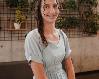 Photo of Classical Kid, Ivy Armendariz smiling and standing in front of a wall of plants.