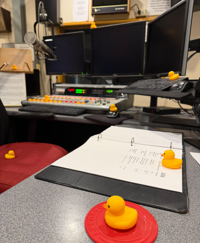 Photo of several rubber duckies left for Jeff Koterba in the studio at KVNO as a surprise on Halloween morning. There's a mixing board, computer screens, and yellow rubber ducks everywhere.