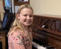 Maggie Dickinson smiling while sitting at a piano
