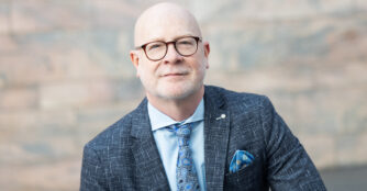 Portrait of Jack Becker, executive director of the Joslyn Art Museum, posing in a blue suit with a happy expression.