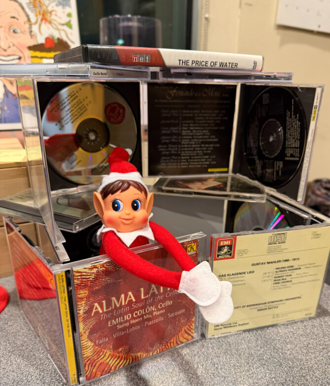 A photo of an Elf on the Shelf in a little fort made of CD cases. 