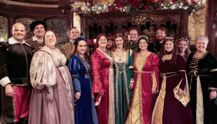 The full Cantare choir poses together in Renaissance attire, standing in rows and smiling toward the camera.