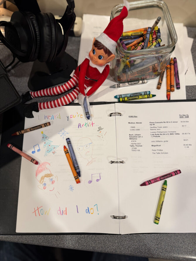 The elf on the shelf in the studio drawing with crayons...he's drawn a self-portrait and one of the morning show host, Jeff Koterba, complete with bald head and glasses.