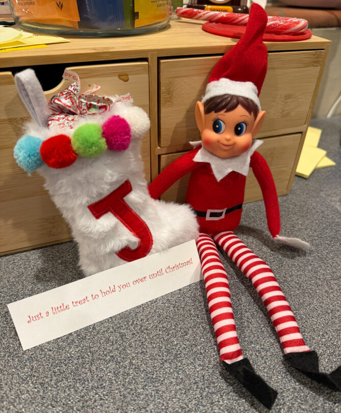 Elf on the shelf with a note that reads: Just a little treat to hold you over until Christmas! There's a little stocking filled with chocolate candies.