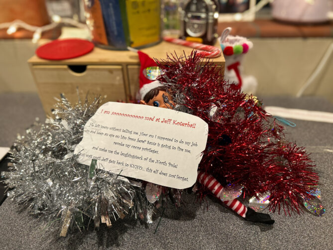 Photo of elf on the shelf, named Ivanhoe, with a note that expresses that he's mad at Jeff Koterba for leaving town without telling him. He's worried that Santa will fire him.