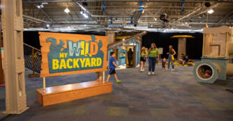 Children and museum staff explore interactive nature displays inside the Omaha Children’s Museum exhibition “My Wild Backyard.”