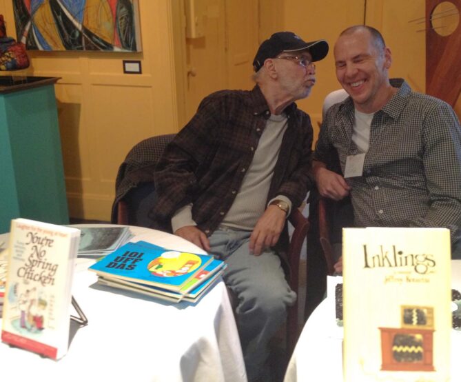 Jeff and Ed Fisher at a book signing. Ed puckers towards Jeff as Jeff laughs. 