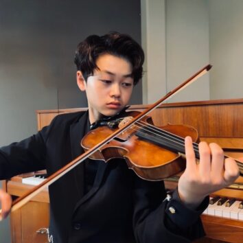 Albert Gwon holding a violin while sitting in front of a piano
