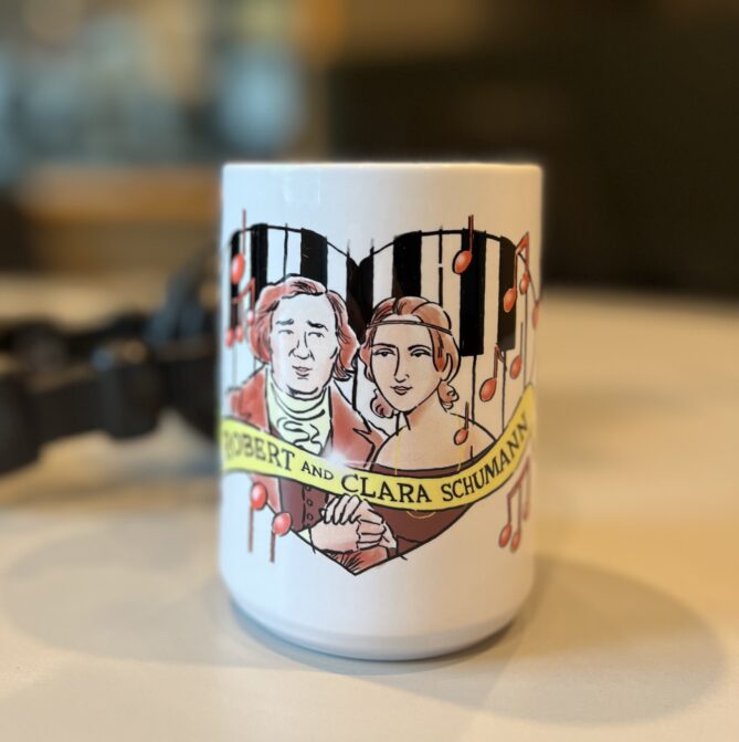 Robert and Clara Schumann mug designed by Jeff Koterba. White mug with a red design. 