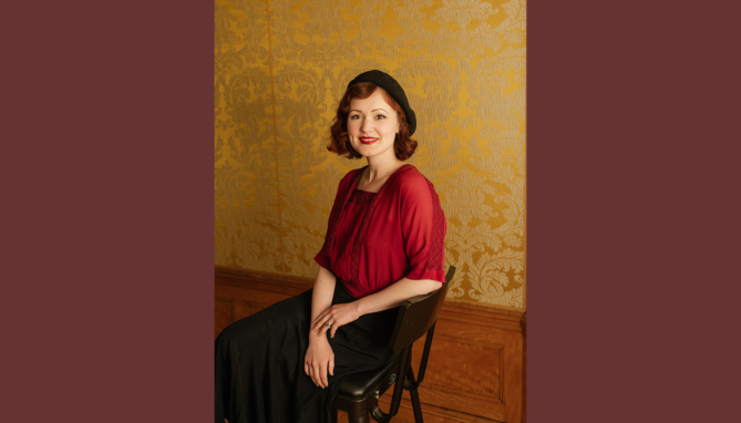 Melissa McCarthy seated and posing for a portrait, wearing a red blouse.