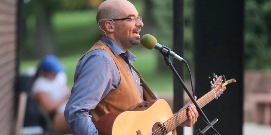 Performer singing into a microphone in a promotional image for A Tribute to John Denver.