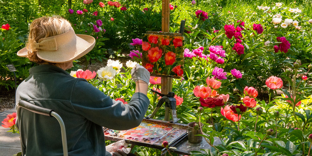 A woman painting in a garden full of flowers