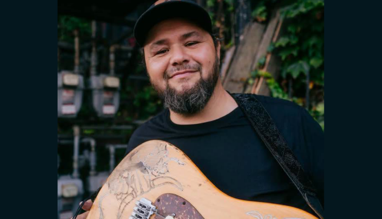 Hector Anchondo poses with his guitar and a light smile.